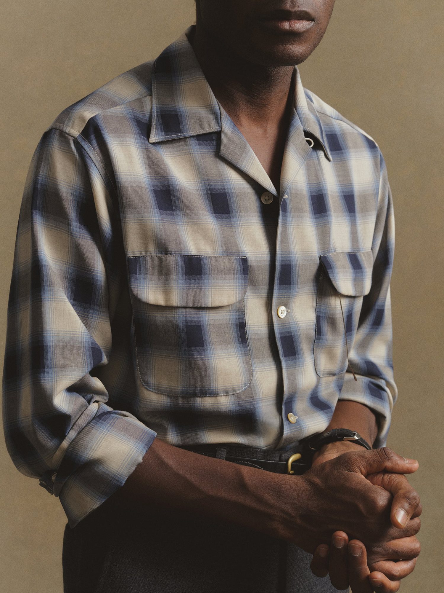 Man in a blue and cream plaid button-up shirt with chest pockets and brown pants