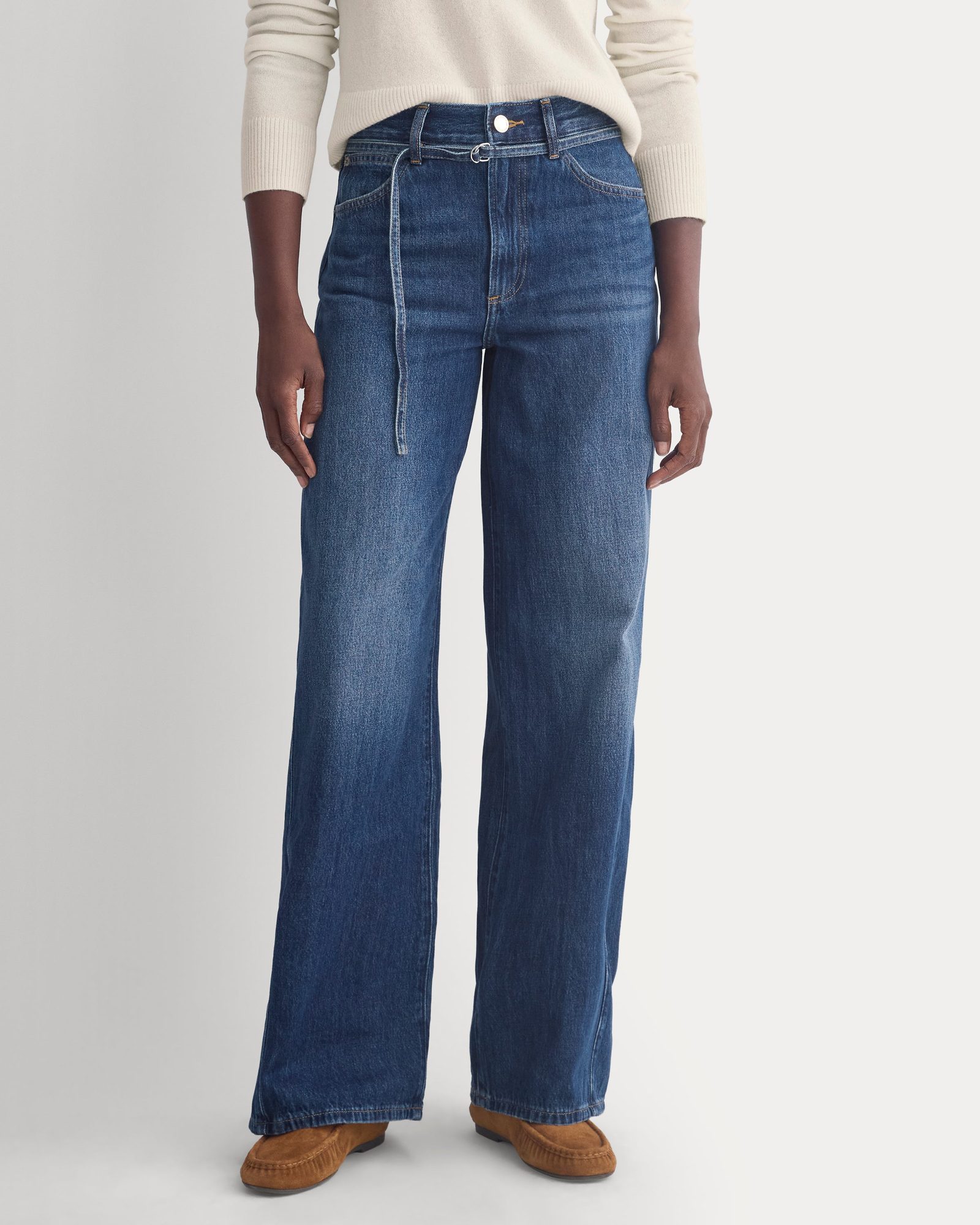 Close-up of woman's lower half wearing cream sweater, blue jeans, and tan slip-on loafers