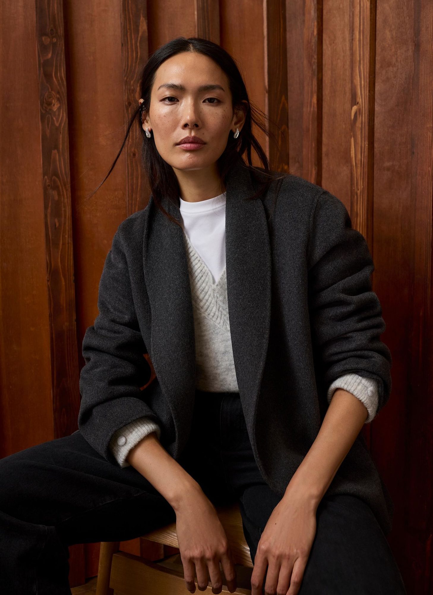 Woman sitting on stool wearing charcoal blazer with cream ribbed sweater and black trousers
