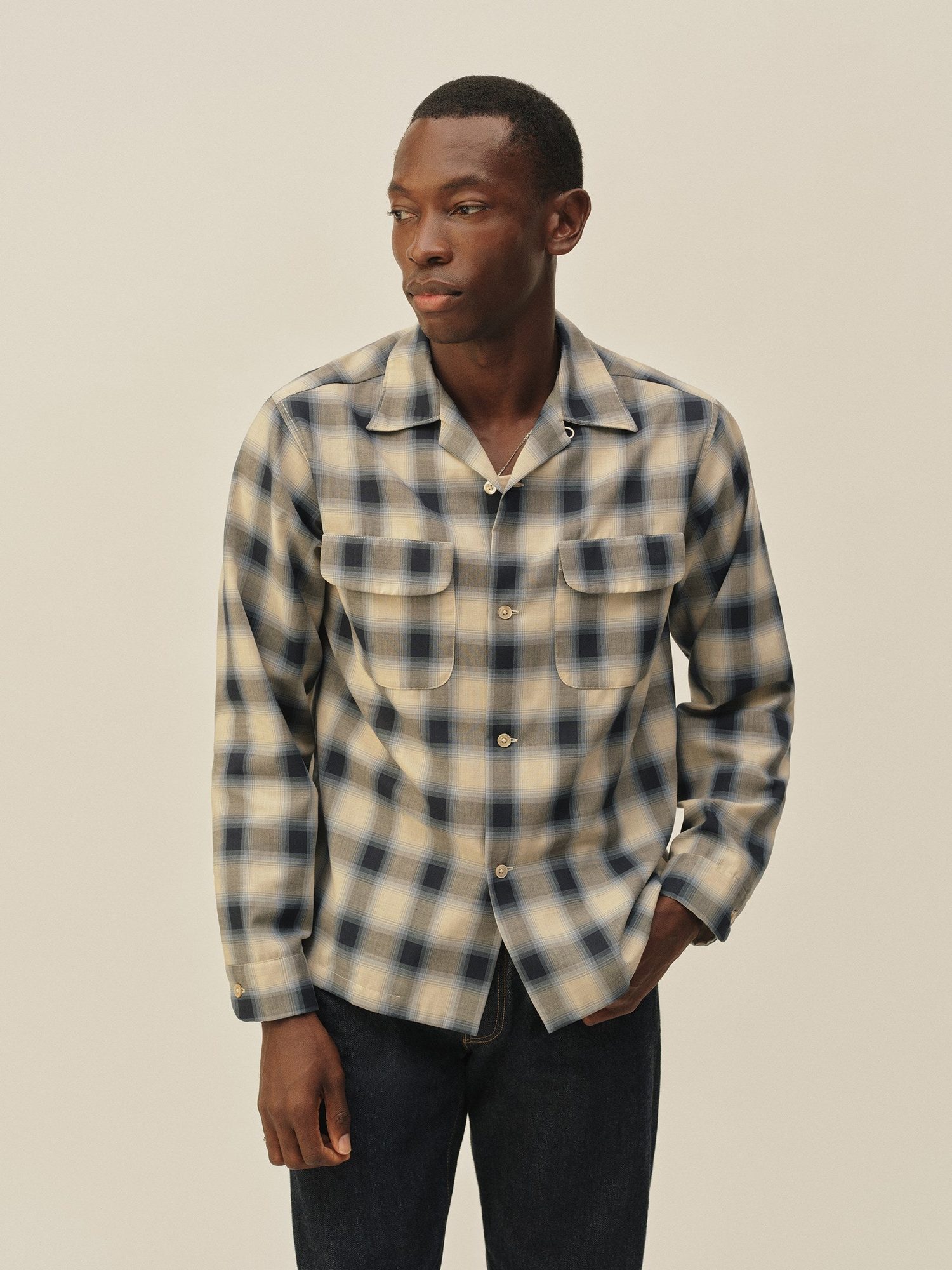 Man wearing a cream and navy plaid overshirt with patch pockets and dark jeans